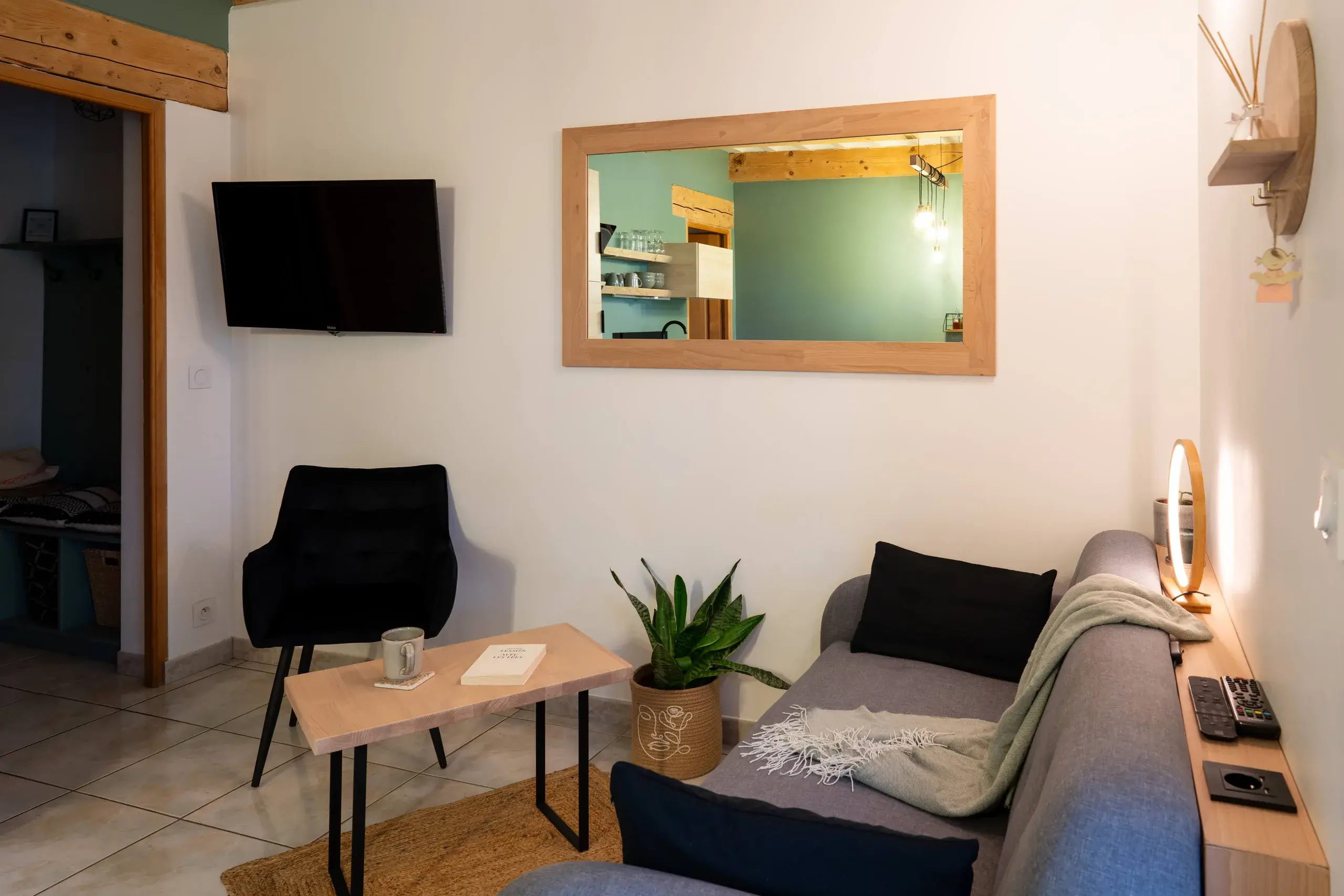 Coin salon dans la pièce de vie avec canapé gris, fauteuil, table basse et télévision