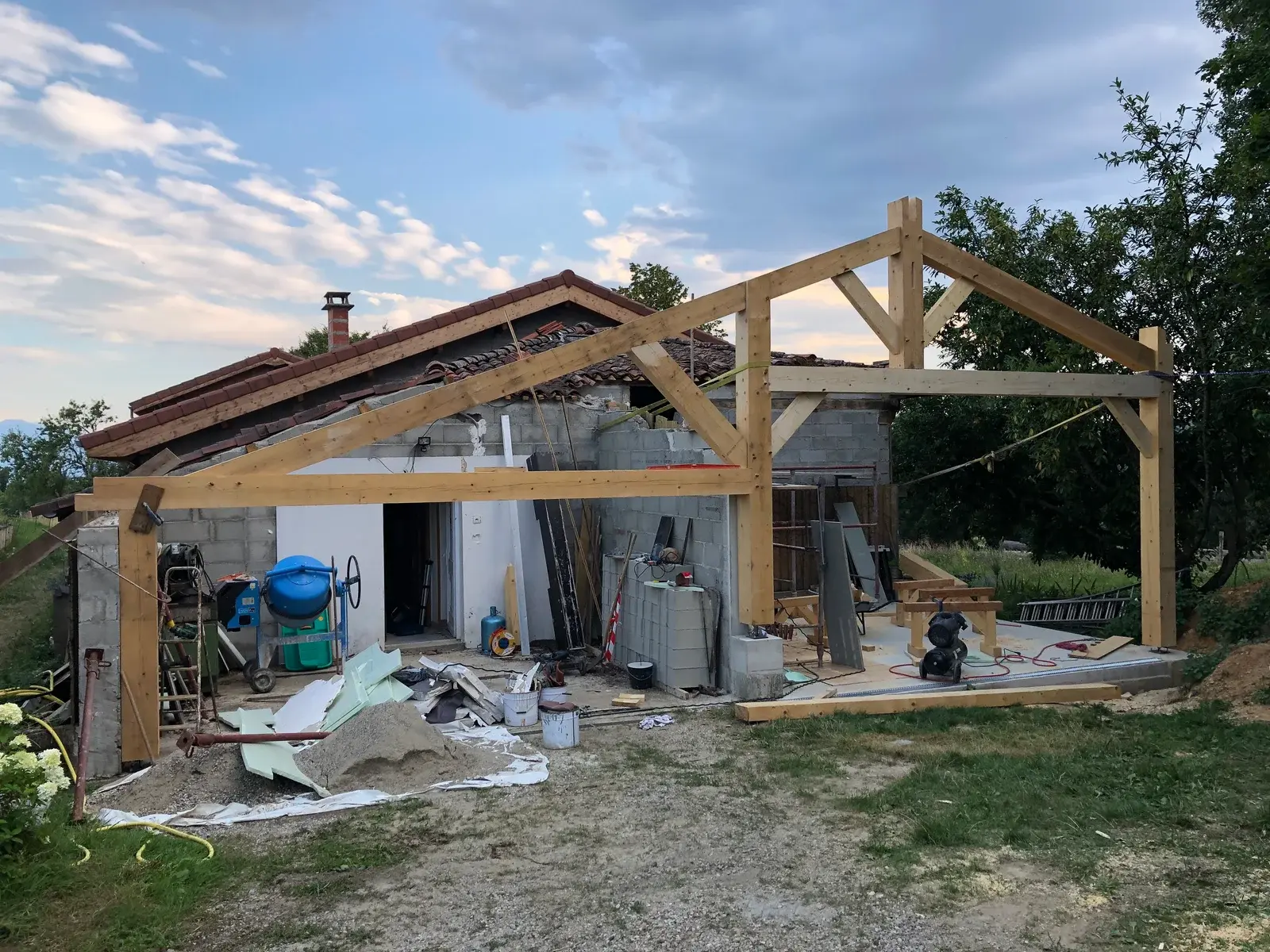La charpente bois du gîte fraîchement levée, structure apparente et matériaux de chantier au sol, en fin de journée