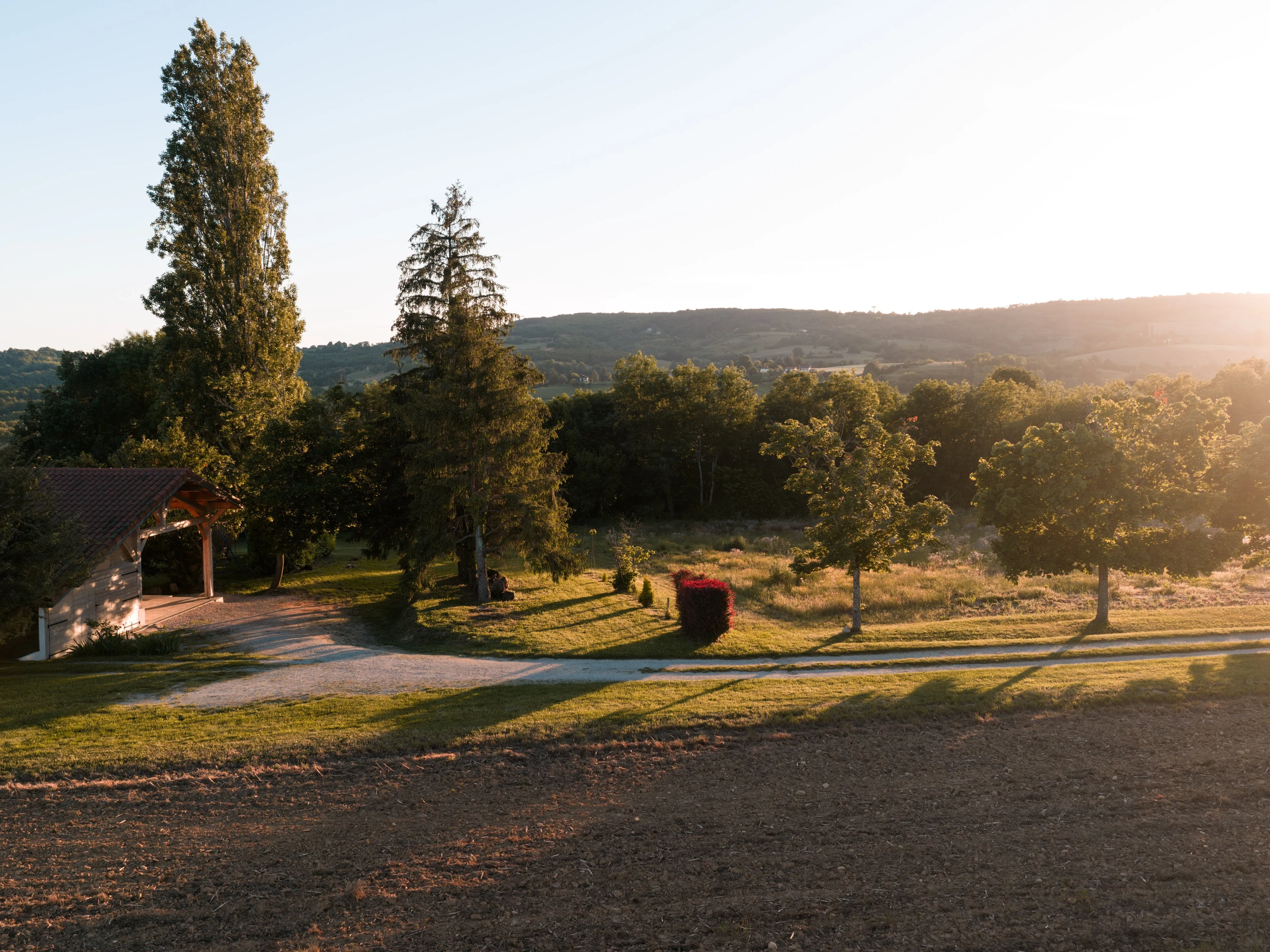 Vue aérienne du domaine L'Hospitalier à l'heure dorée — allée d'entrée, jardin et collines