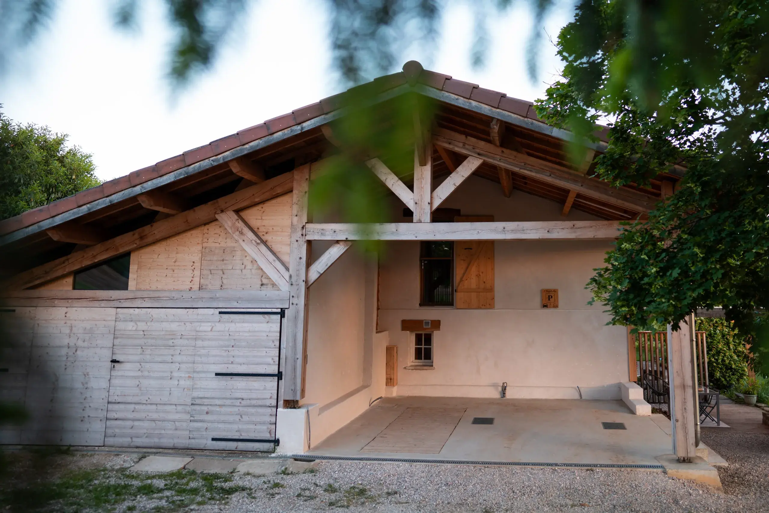 Entrée couverte du gîte L'Hospitalier avec charpente en bois taillée par Arnaud et abri voiture