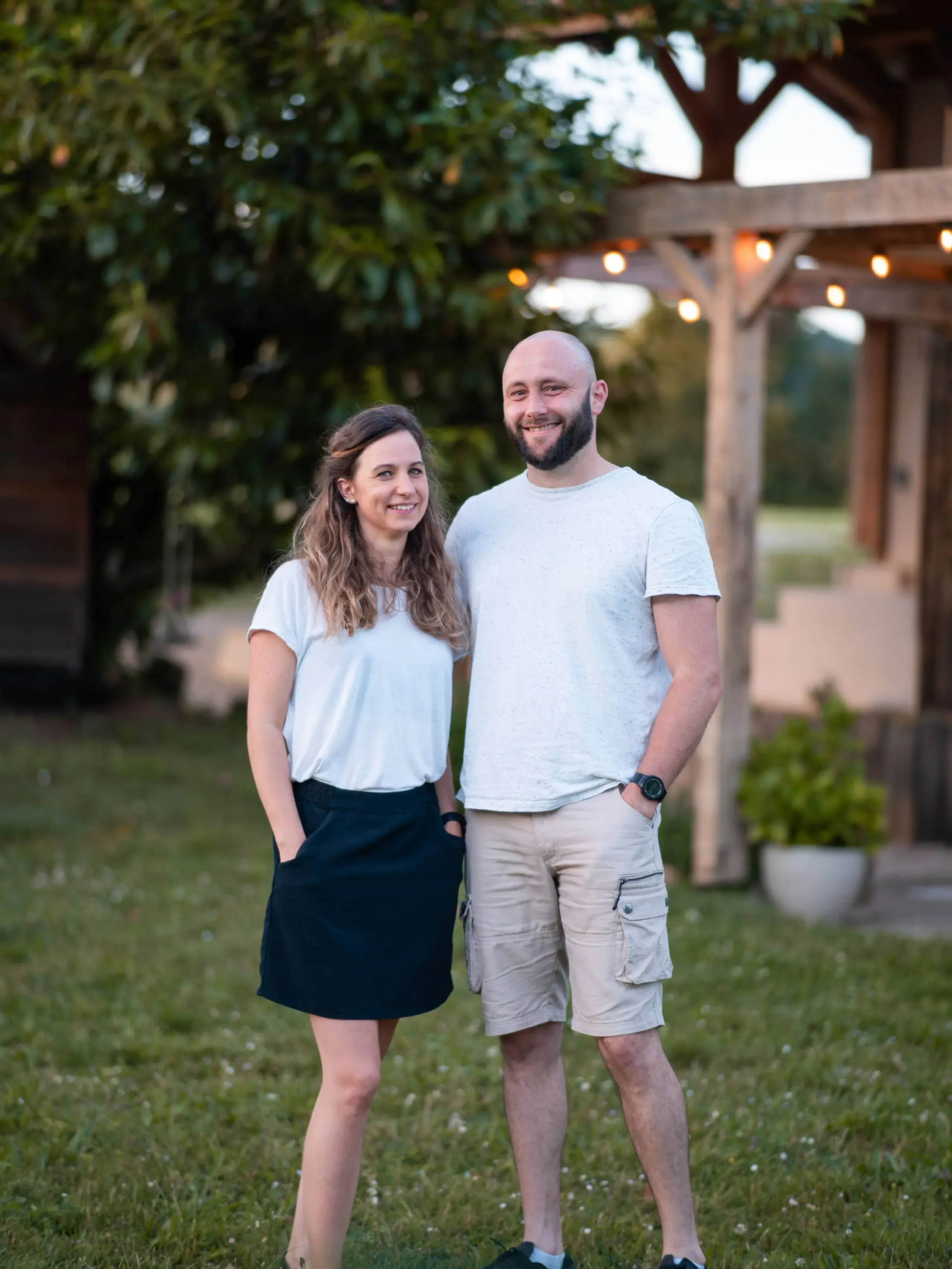 Esther et Arnaud devant le gîte illuminé au crépuscule, charpente bois et guirlandes en arrière-plan