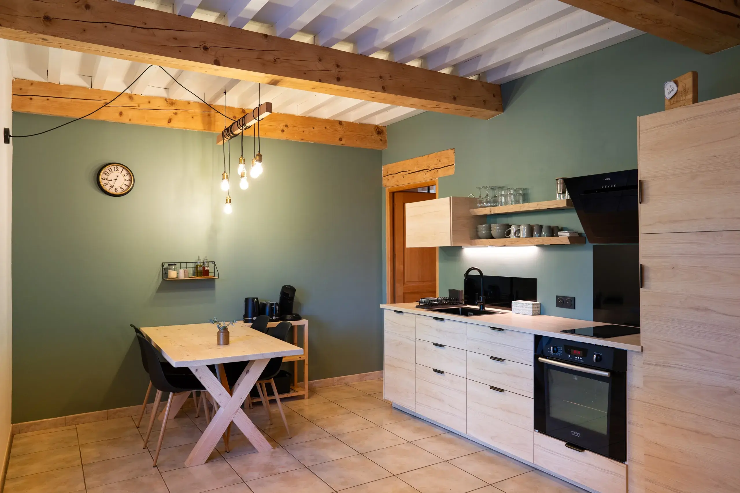 Cuisine equipee du gite avec table a manger, poutres apparentes et mobilier en bois clair
